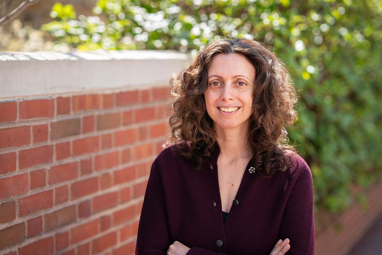 Elena Fratto beside a brick wall with green foliage.