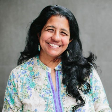 Professor Aparna Venkatesan standing by a gray wall.