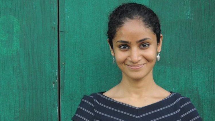 Divya Cherian standing in front of a green wall.