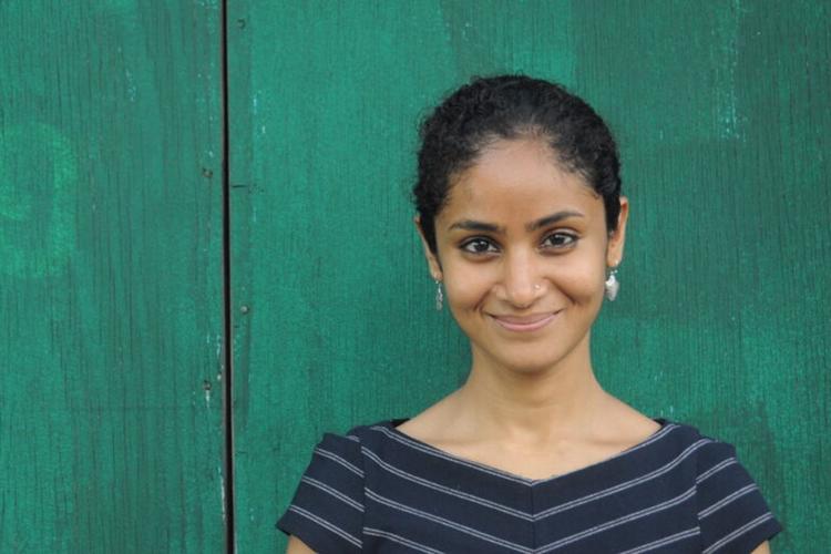 Divya Cherian standing in front of a green wall.